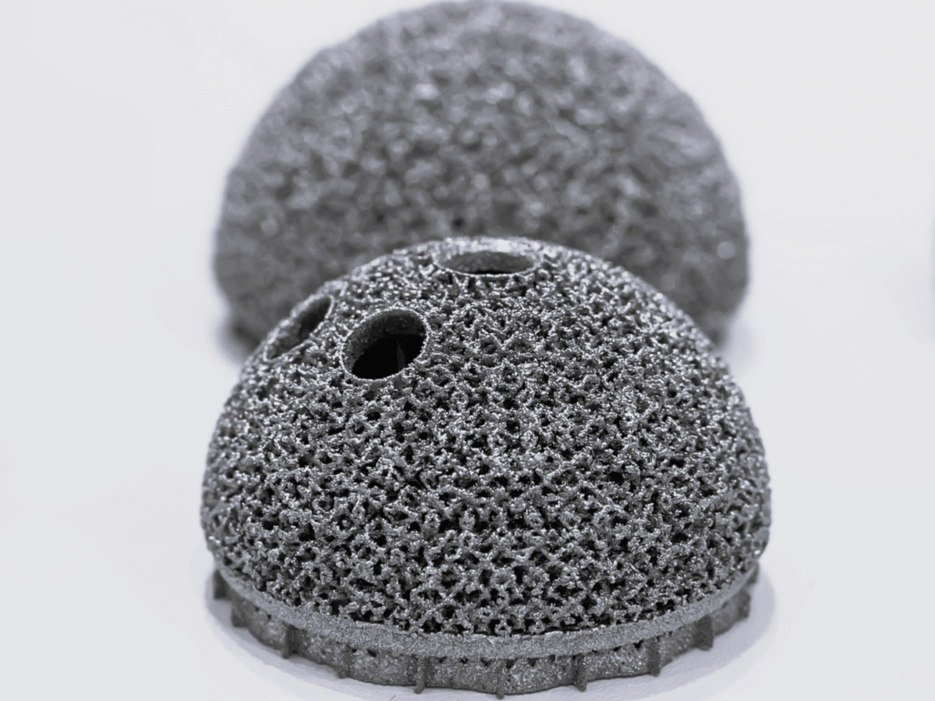 Two metallic, porous, dome-shaped objects with holes rest on a smooth, light surface.