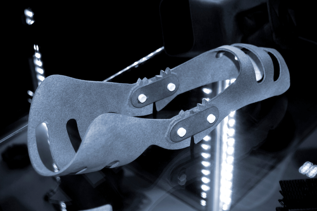 A flexible, textured brace with circular cutouts and riveted connectors on a reflective surface lit by vertical LED lights.