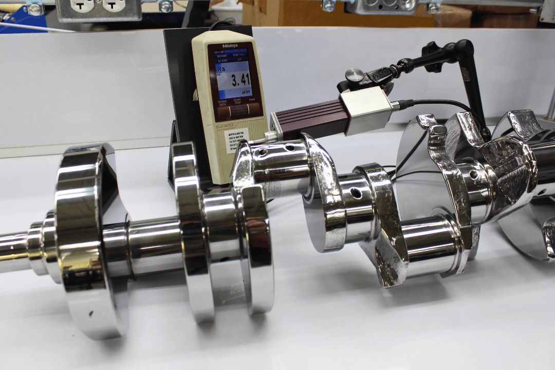 A chrome crankshaft is measured by a handheld device displaying "Ra 3.41 µin" in a mechanical workshop setting.