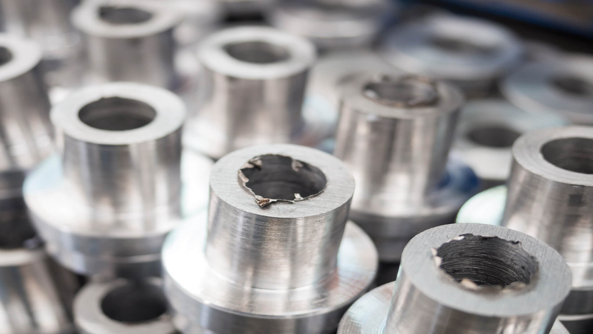 Metal cylinders stacked together, displaying rough, unfinished edges in a workshop setting.