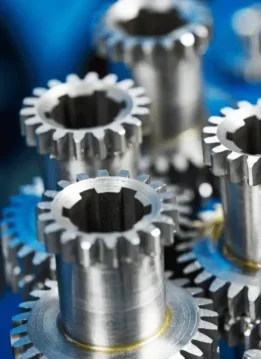 Metal gears are positioned upright, interlocking with one another, in a workshop setting with a blurred blue background.