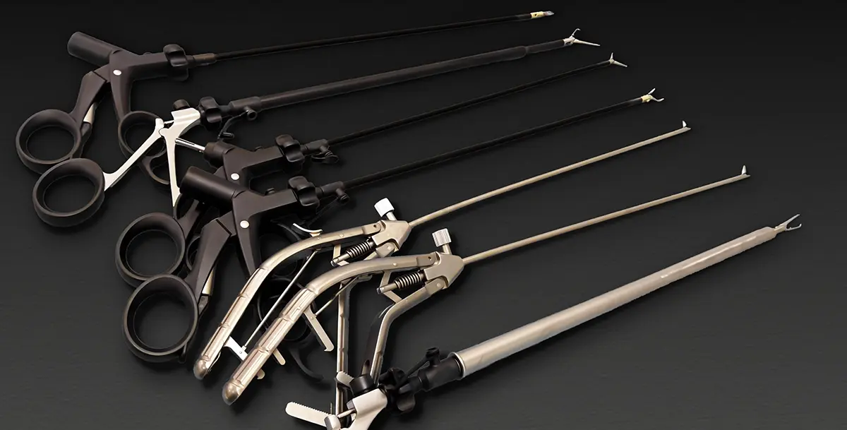A set of long, slender laparoscopic surgical instruments with scissor‑style handles arranged on a dark surface. The tools have metal shafts and small end effectors used for grasping or cutting during minimally invasive surgery.