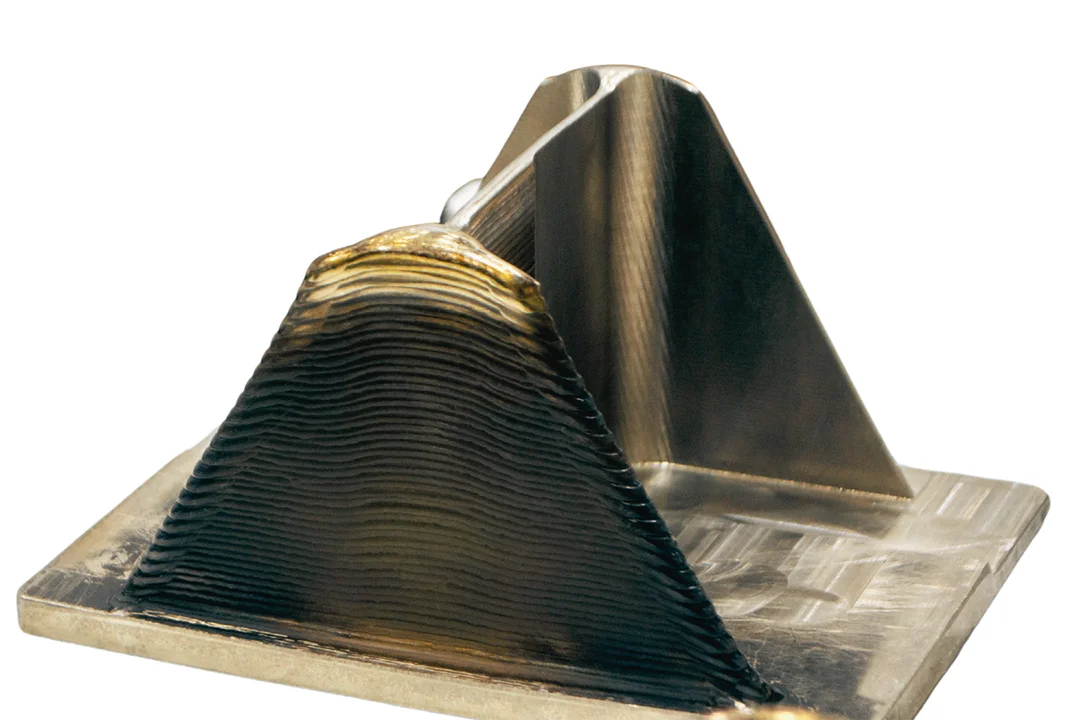 A 3D printed pyramid shaped support on a square base, showcasing printed texture and varying shades of bronze prior to post-processing.
