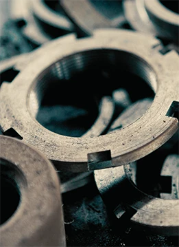 Metal washers lie stacked and overlapping, their surfaces rough, with heat treat scale, scattered on a dark, industrial surface.