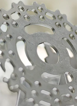 An upright metal plate showcases intricate circular patterns and cutouts with sharp edges against a blurred industrial or mechanical background.